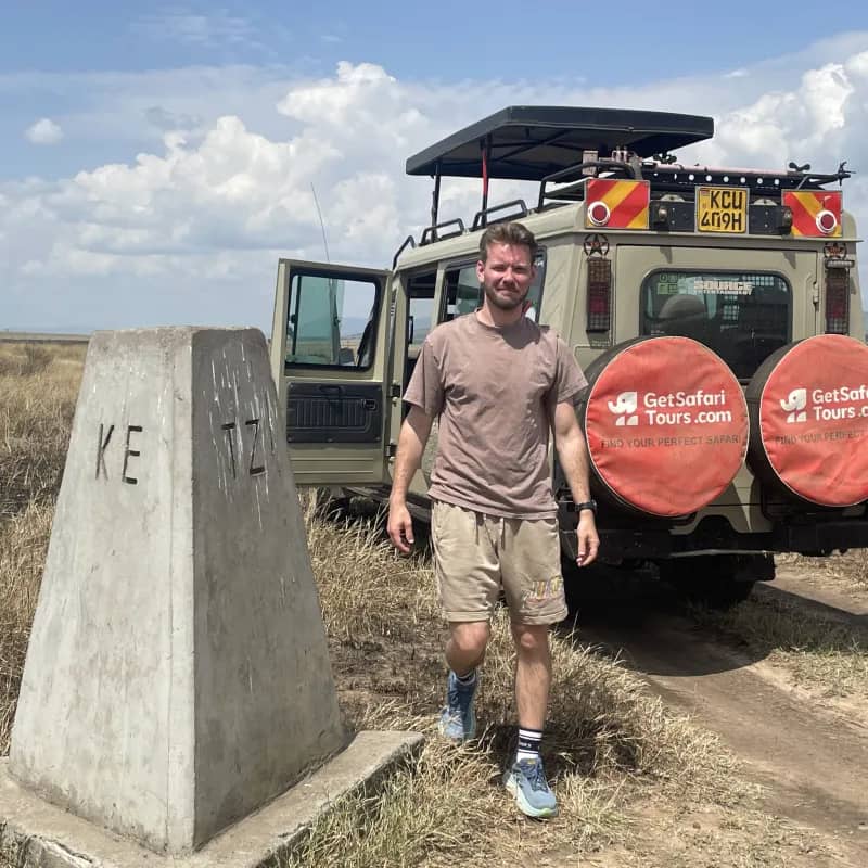 Karlis at the Kenya–Tanzania border post with the branded safari vehicle behind