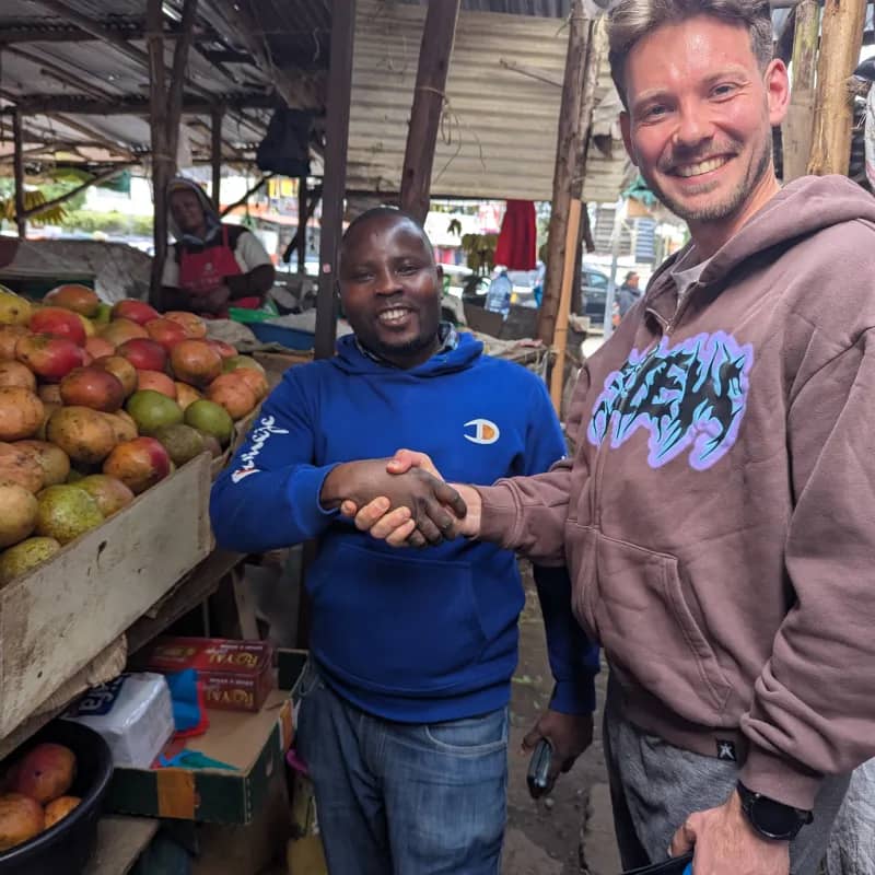Karlis shaking hands with a fruit seller at a local market