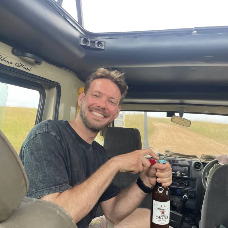 Karlis in the safari vehicle with the roof popped, opening a local beer